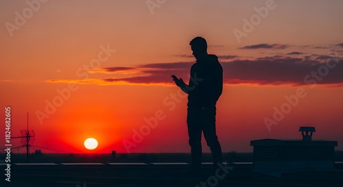 Silhouette of a person holding a phone against a vibrant sunset sky