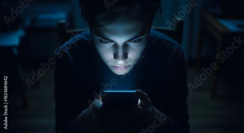 Young person illuminated by smartphone screen in dark room