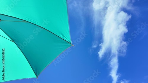 Beach umbrella swaying in the wind against a bright blue sky, evoking peace, relaxation and vacation vibes.