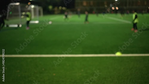 Night view of a football training session on an artificial turf field under bright floodlights with small goals and cones set up for youth practice.
