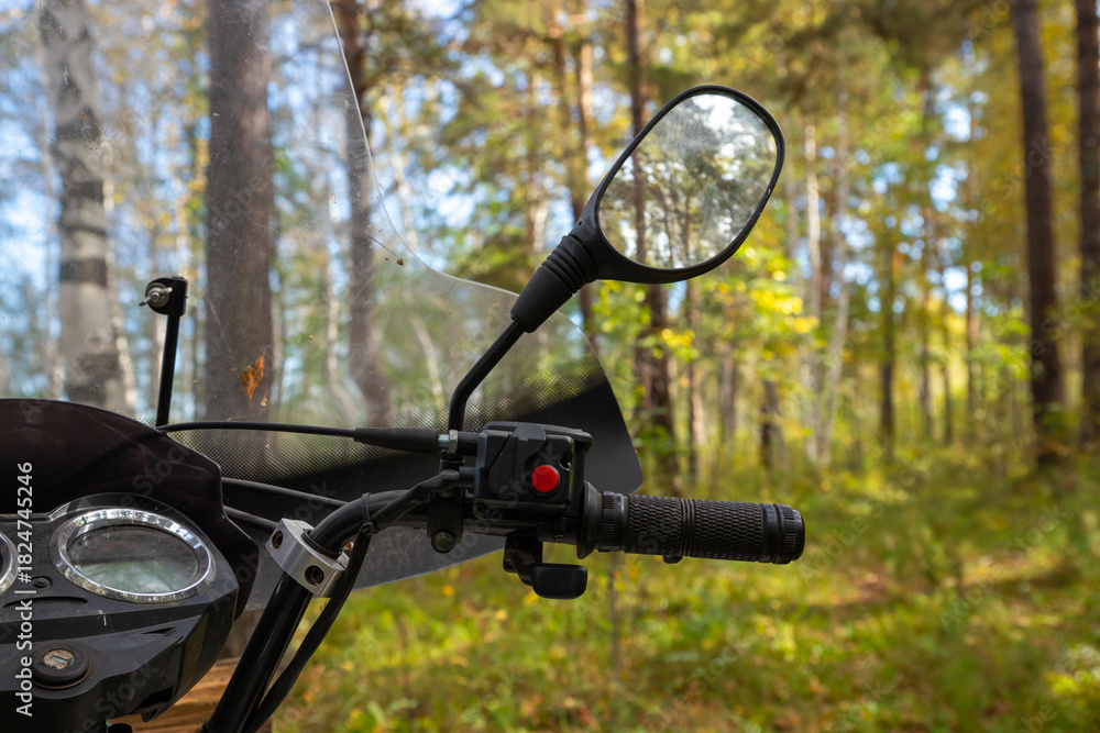Fototapeta premium right handlebar, throttle handle, ATV windshield, steering wheel and rear view mirrors. Quad bike or ATV stands idle among tall trees and lush greenery