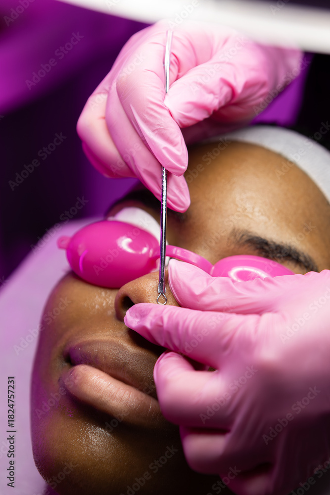 Fototapeta premium African woman in beauty clinic doing a facial evaluation and a cosmetology treatment. Woman on an esthetician appointment of facial. use mask do skincare routine