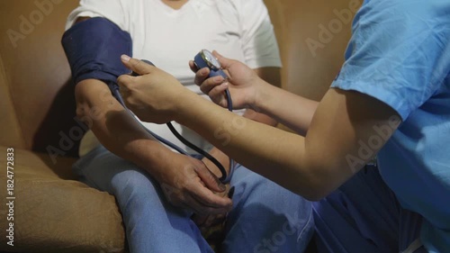 Nurse taking the blood pressure of a woman sitting on a sofa in a living room.