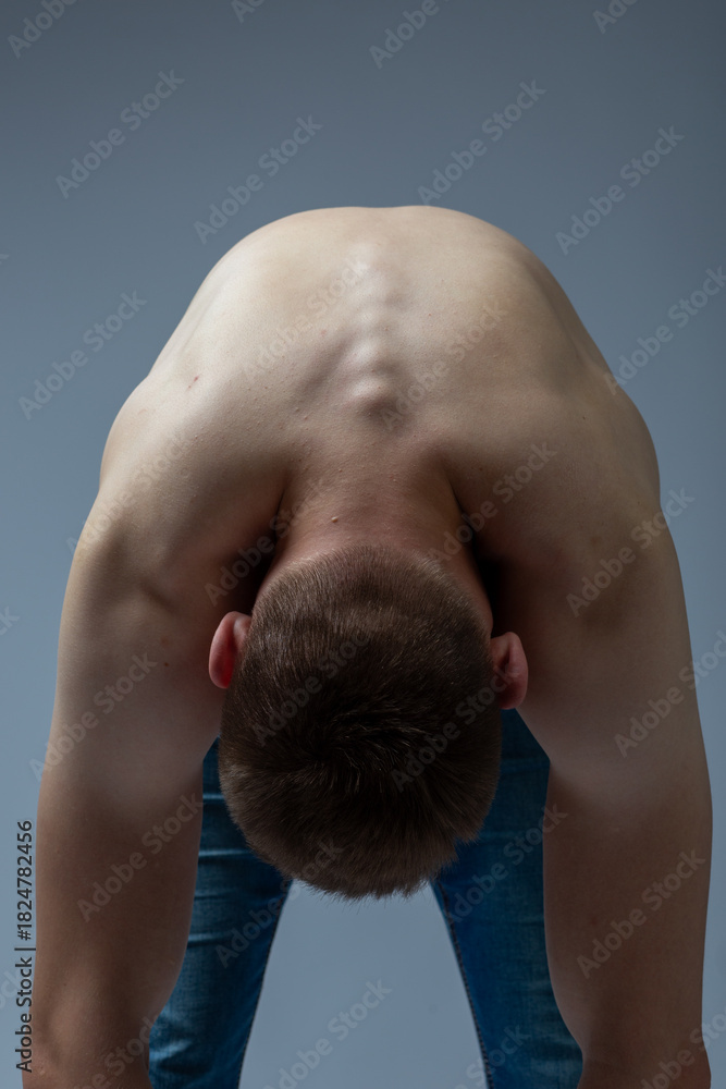 Naklejka premium A young man bends over and demonstrates his spine. Cervical spine. Concept: yoga, stretching, and morning exercises. clear back skin without teenage acne