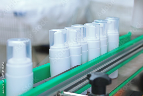 White plastic bottles move along the conveyor belt. Manufacture of cosmetics and skin care products. A capping and labeling machine.