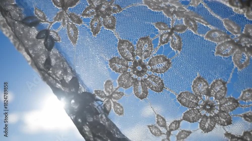 Close-Up of White Lace Fabric With Floral Patterns Against a Bright Blue Sky with Sun Glare