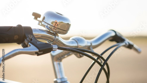 Close-up of bicycle handlebar with bell and brake cables, shallow depth of field, bright sunny background.