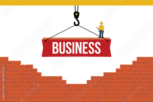 A worker supervises as a crane lifts a banner that says "BUSINESS" over a construction site with a brick wall.
