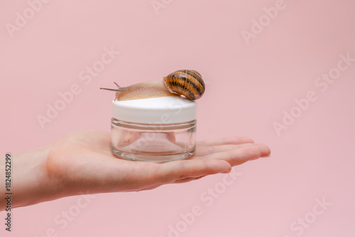 Glass cosmetics bottle with snail in woman's hand. Mockup for brand. Skin care product, spa, luxury, natural beauty cream