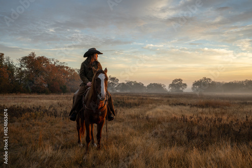Woman Wearing Cowboy Hat Riding Horse and Looking Off At Golden Hour of Sunset With Cloudy Sky