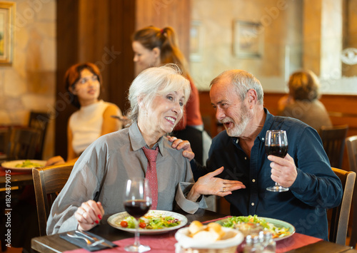 фотографія Happy senior couple enjoying relaxed dinner together in cozy restaurant while ta