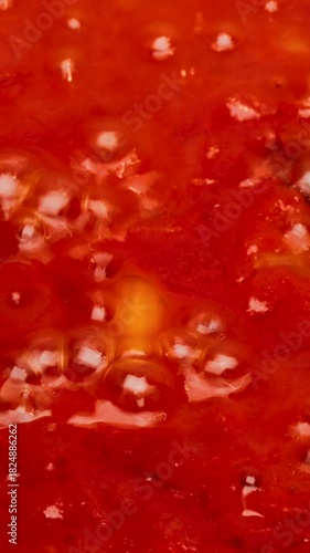 Vertical video. Close-up of boiling red tomato sauce with visible spices and ingredients, captured in a vertical format while preparing homemade ketchup or sauce