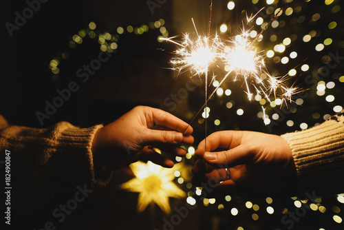 Happy New Year! Burning sparklers in hands on background of christmas tree golden lights bokeh at night. Glowing fireworks in couple hands, new year eve holiday celebration
