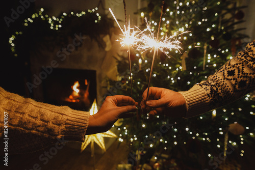 Happy New Year! Burning sparklers in hands on background of christmas tree golden lights at night. Glowing fireworks in couple hands, new year eve holiday celebration