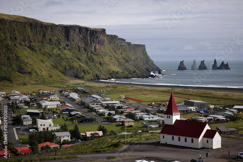 Picturesque icelandic coastal village nestled beneath dramatic green cliffs with sea stacks in the distance