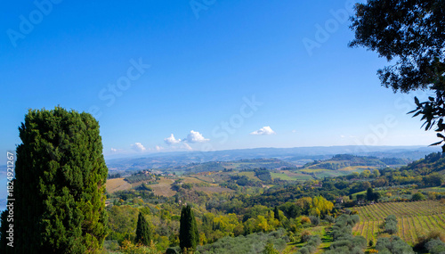Panoramic Tuscan Countryside With Rolling Hills, Vineyards, and Tall Cypresses Under a Bright Blue Sky