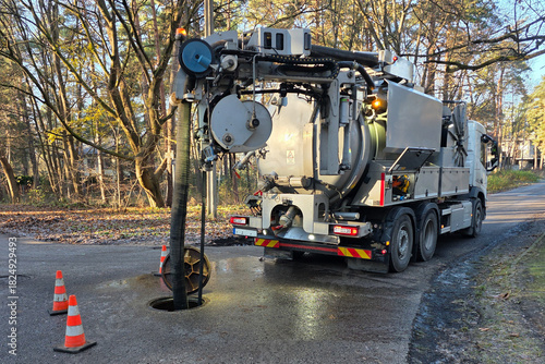 Hydro-vac sewer cleaning truck servicing underground pipeline through open manhole on a forest road