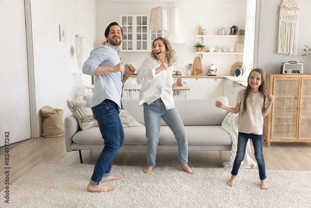 Fototapeta premium Overjoyed parents with little daughter jump dance in bright apartment