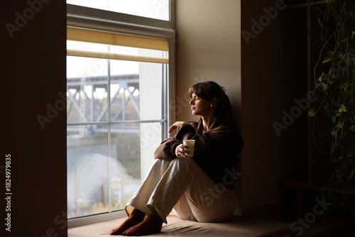 Pensive woman enjoying a quiet moment by the window with a warm drink