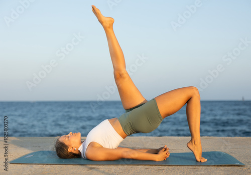 Athletic girl training bridge position on blue mat in open air by the sea