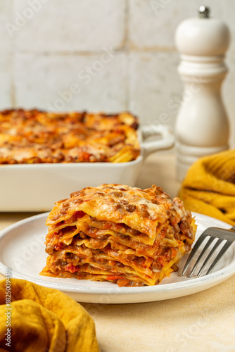 Close up of slice of homemade Red Lentil Lasagne. Vegetarian dish made layered sheet pasta, with vegetables, lentils and tomato ragu and is topped with a creamy cheese topping. Vertical image.