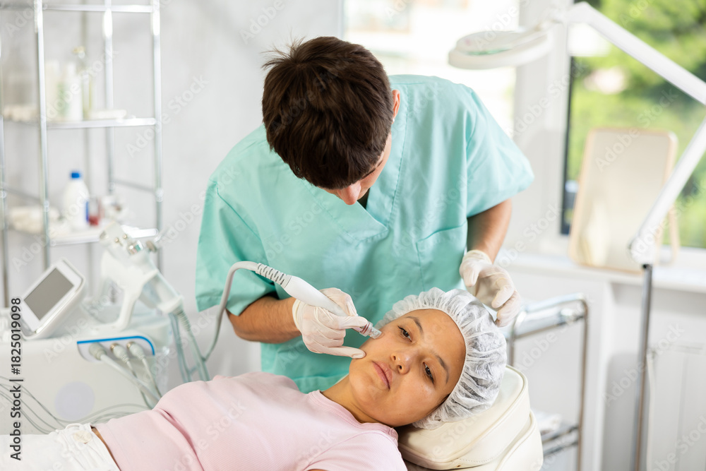 Obraz premium Young male cosmetologist performs facial cleansing procedure for young woman client