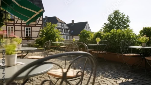 Outdoor cafe with iron chairs, round tables, and plants in pots on a sunny terrace