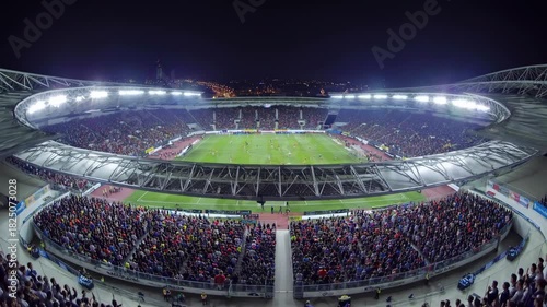 Aerial video shot of a vibrant, illuminated stadium at night, capturing a dynamic sports event with a wide-angle view of the bustling crowd.