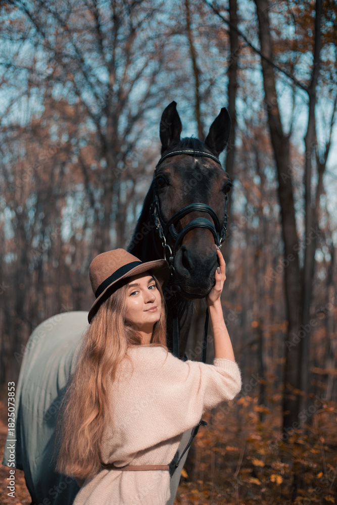 Obraz premium Woman stands beside horse in forest during fall season while wearing a hat and sweater