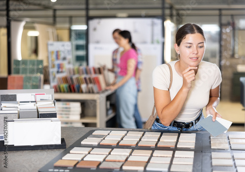 Tablou pe pânză Enthusiastic young woman exploring various natural and technical stone tile samples presented on display board in building hypermarket to find perfect match for home renovation project