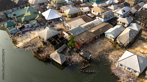 Aerial view of houses lining a polluted shoreline, with traditional boats afloat on the water, creating a stark contrast, Bolo Town, Rivers State, Nigeria
