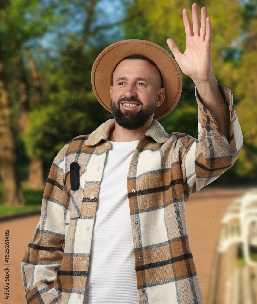 Obraz premium Man with hidden spy camera waving hand to someone outdoors