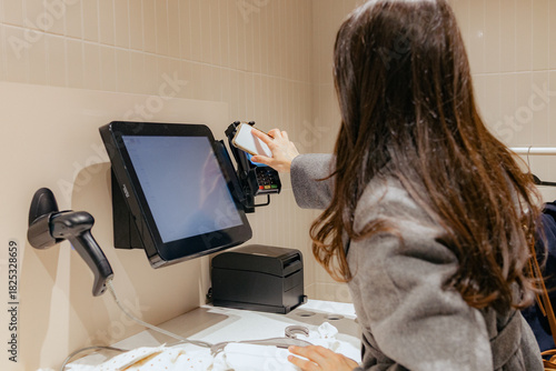 A girl makes a payment using a mobile phone at the checkout in a store.
