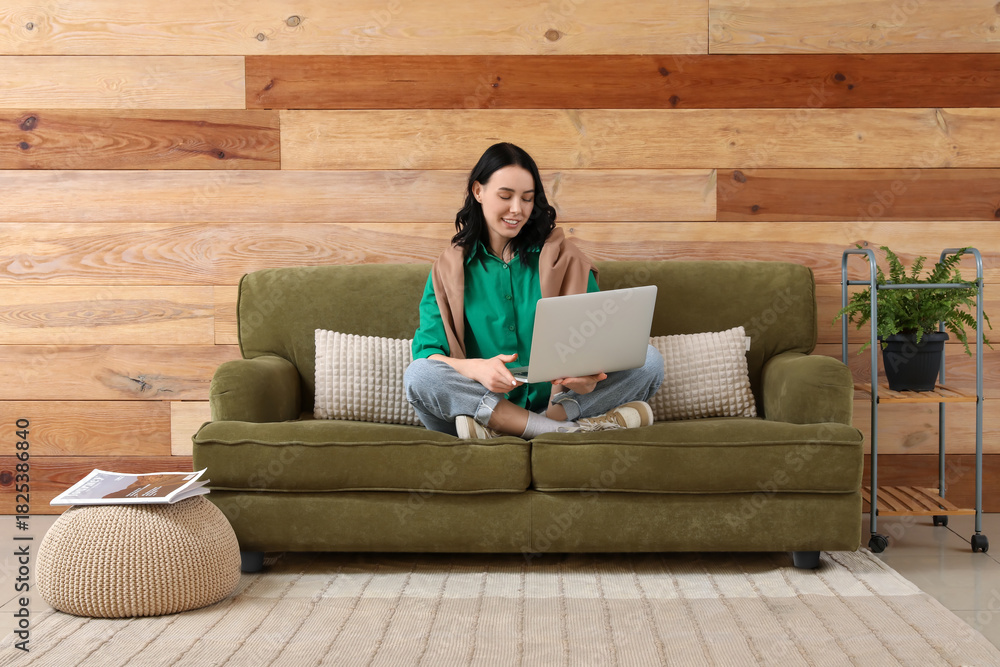 Obraz premium Pretty young woman using modern laptop on green couch at home