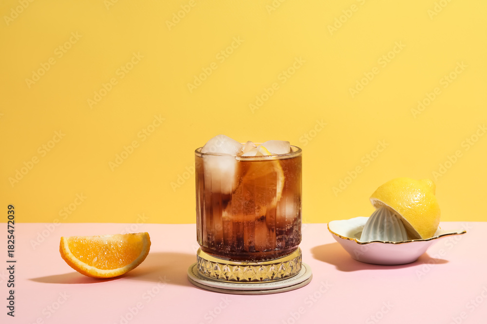 Obraz premium Glass of Long Island iced tea cocktail and juicer on pink table against yellow background