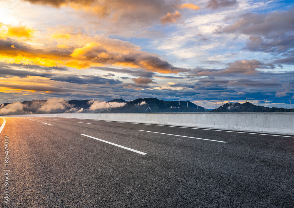 Obraz premium Empty asphalt highway road and mountain with wind turbines landscape at dramatic sunrise