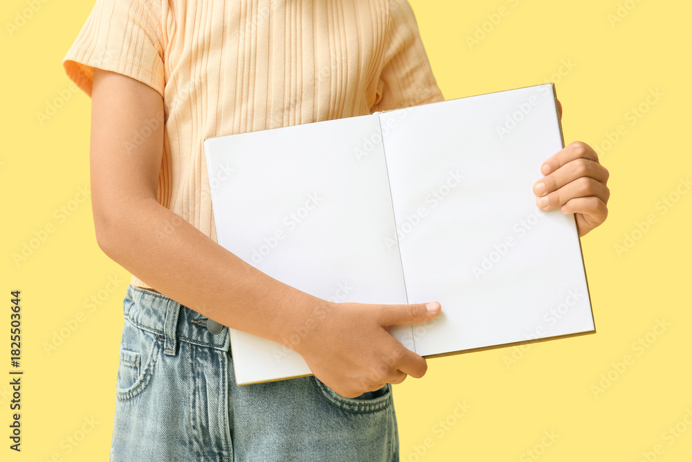 Fototapeta premium Cute little girl holding open blank book on yellow background