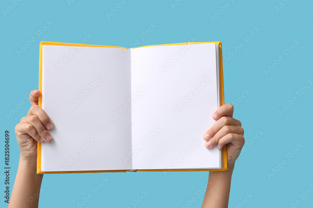 Naklejka premium Hands of little girl holding open blank book on blue background