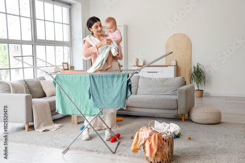 Φωτογραφία Young mother with cute little baby hanging laundry on drying rack at home