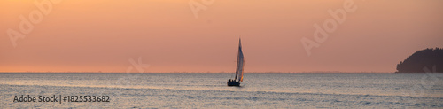 Peaceful recreation sailing in of the Pacific Coast in small sailboat at sunset, pastel sky in yellow an orange against blue water
