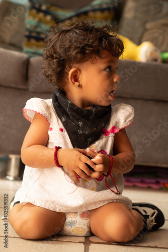 Cute toddler mexican girl with curly hair sitting on floor indoors