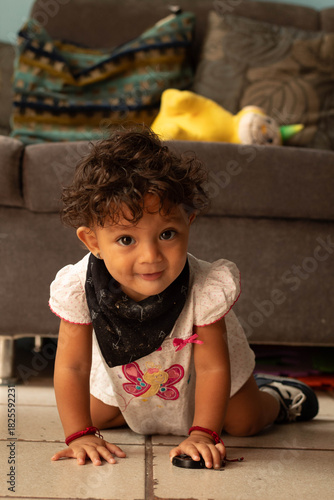 Cute toddler girl with curly hair crawling on living room floor