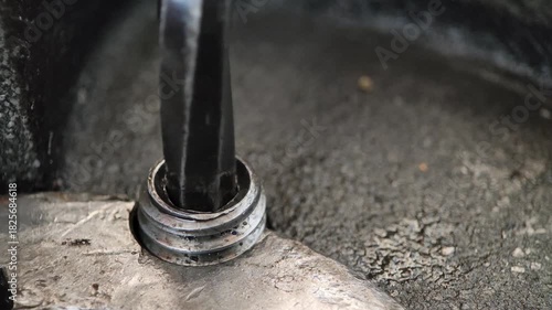 Close-up of a metal L-shaped hex key (Allen wrench) being used to tighten or loosen a hex socket bolt in a gritty, industrial, or mechanical assembly, highlighting repair work.
