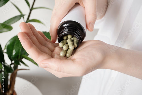 Female hands pouring supplements from a bottle, promoting health and wellness