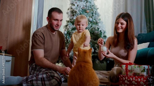 family pet joy, warm family scene with playful cat and festive decorations, happy family spends joyful moment with feline near decorated holiday tree with wrapped gifts