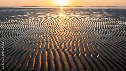 夕焼け空の下、砂浜の波模様が美しいグラデーションを描き出す風景。穏やかな海と空が広がる、静寂な自然の瞬間。