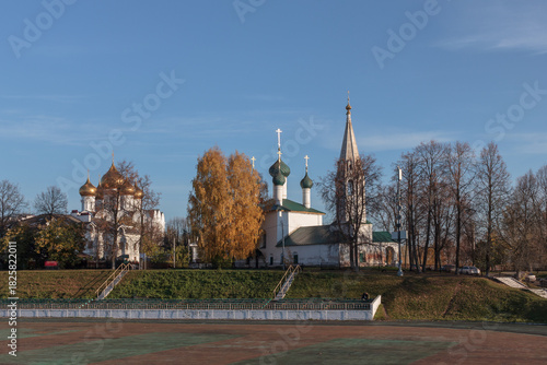 Historic churches in Yaroslavl under blue sky with autumn trees and green lawn.
