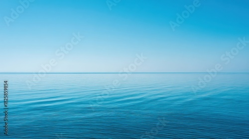Calm blue ocean stretches toward the horizon blending with a clear bright sky. Gentle waves create a serene atmosphere reflecting sunlight on the water's surface.
