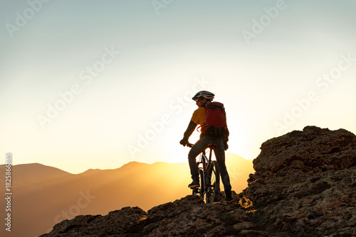 Mountain biker man is standing with MTB bike against sunset sky at mountain top