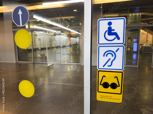Set of accessible signs at entrance with sliding glass doors. Designating accessible area for wheelchair users, as for deaf and blind individuals. Accessible area concept for handicapped people